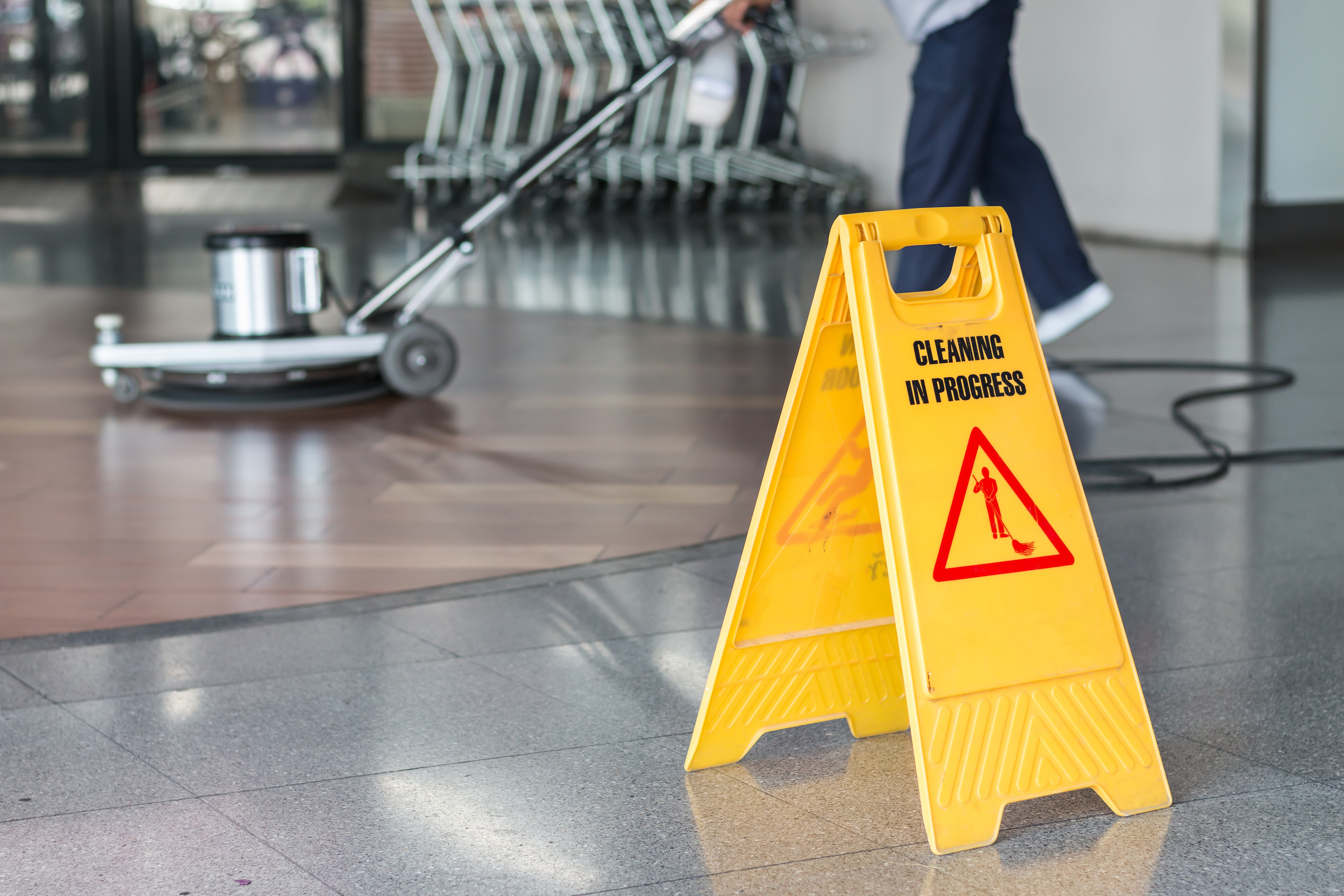 Yellow wet floor sign with "CLEANING IN PROGRESS" text and warning symbol in commercial building hallway
